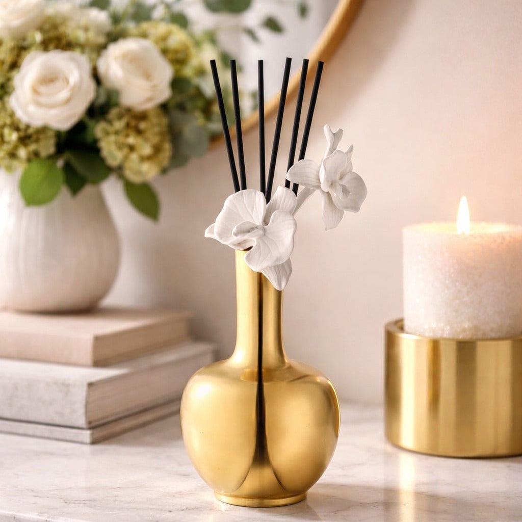 Gold vase Diffuser with black reeds and white flowers on a marble surface with books and a candle - Waterdale Collection