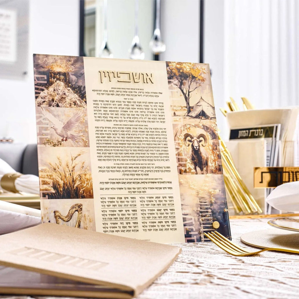 Painted by Batya Ushpizin tabletop plaque displayed on white table with gold cutlery, featuring Hebrew text and golden botanical illustrations for Sukkot
