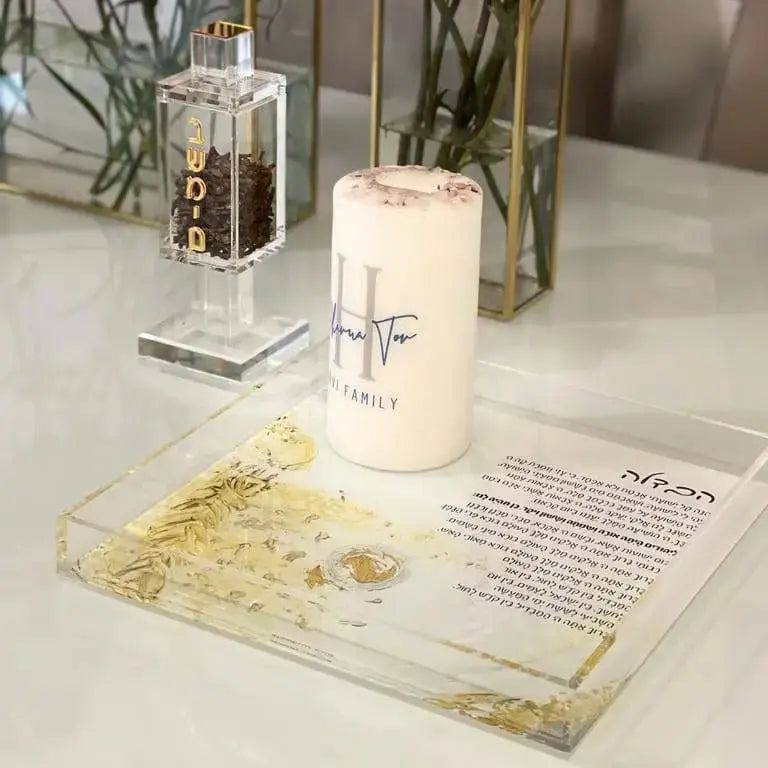 Painted gold Havdalah plate displayed on white surface with ceremonial items, showing delicate gold leaf design on clear glass tray for Shabbat blessings.