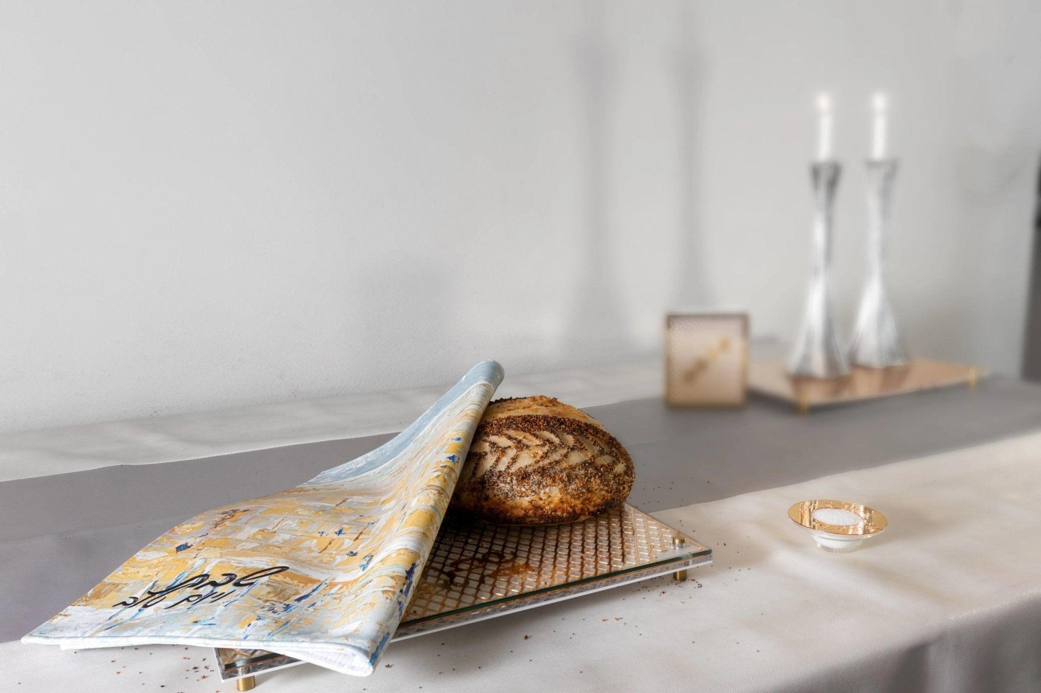 Gray and gold painted leather Challah Cover from Waterdale Collection displayed on table with bread and Shabbat items.