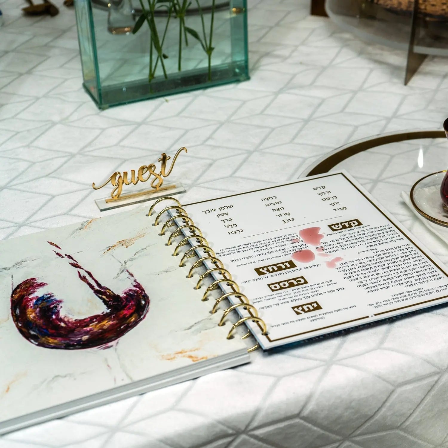 Painted Krias Yam Suf Haggadah displayed on marble surface with planner and gold accessories nearby