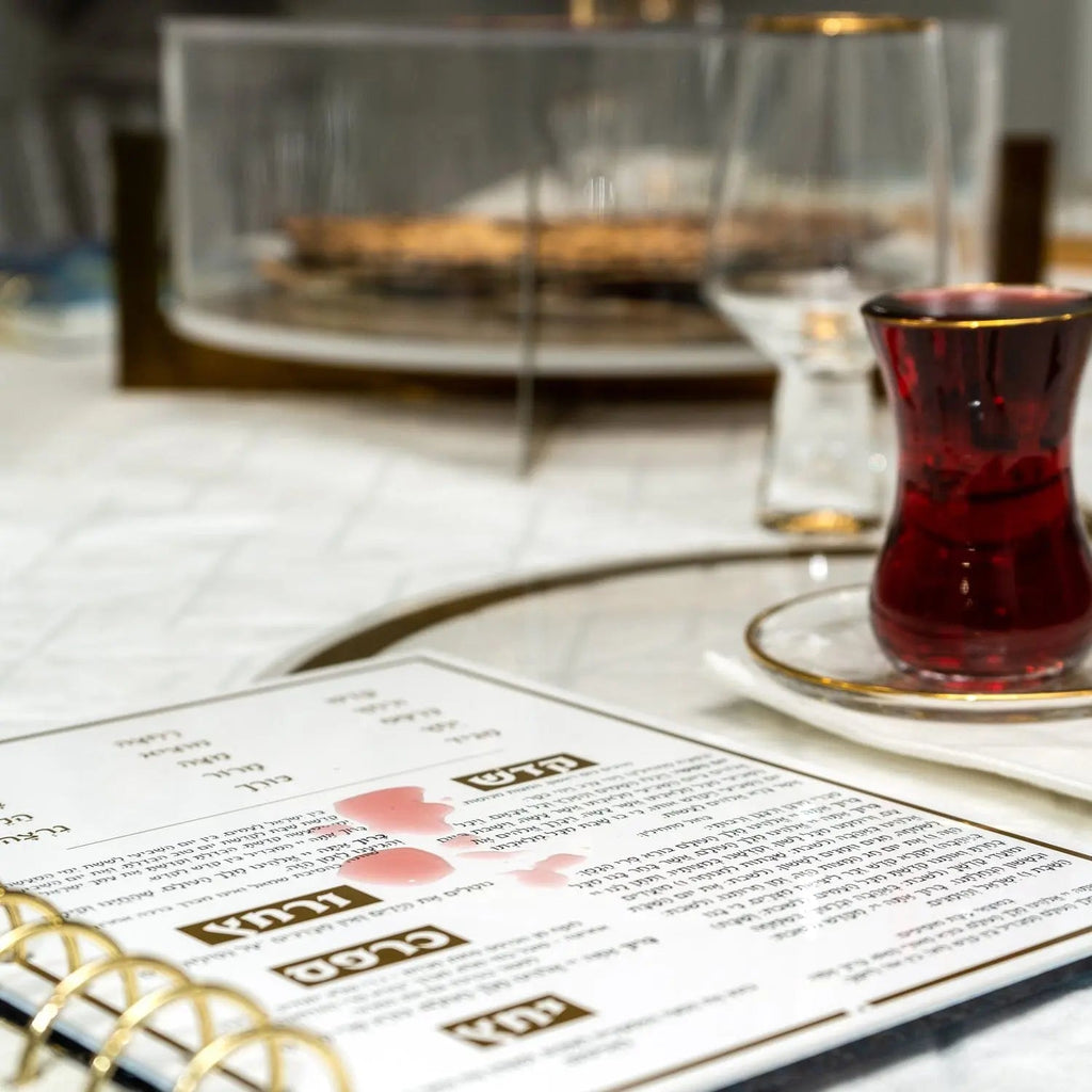 Painted Krias Yam Suf Haggadah displayed on a desk with a cup of tea and prayer book nearby