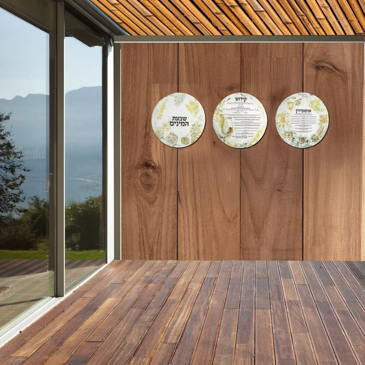 Three round painted ceramic plates hung on wooden sukkah wall decoration, displayed in modern covered porch setting with forest view.
