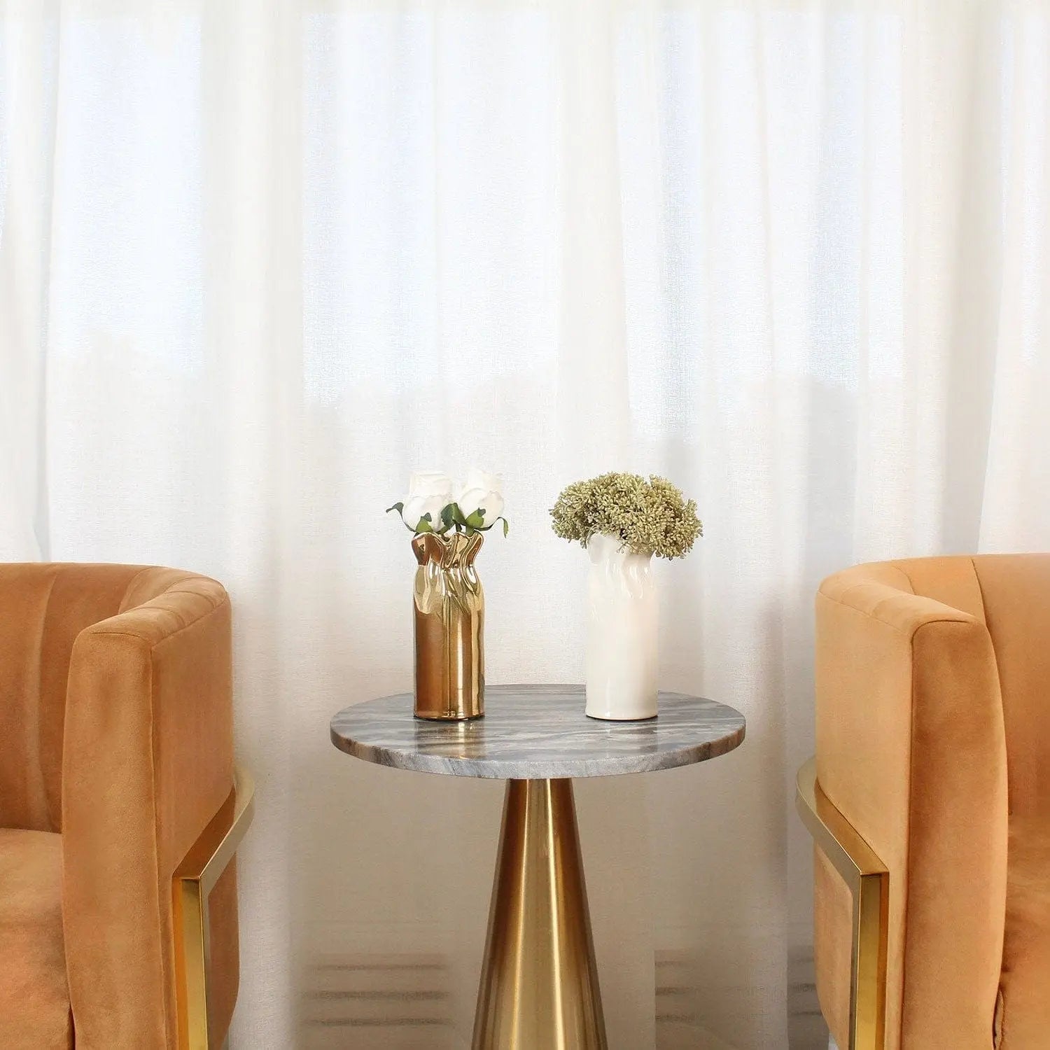 Gold Paper Bag Faux Floral arrangement in brass vase on round table with two tan chairs and white curtains behind