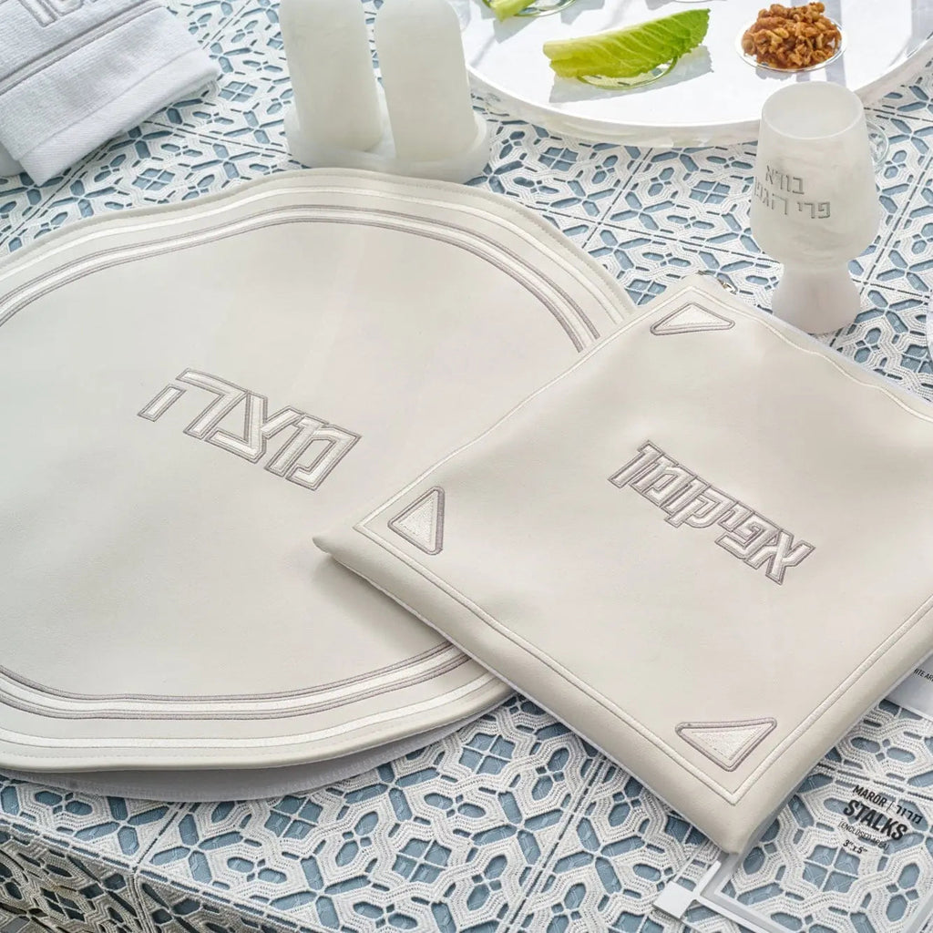 Pearlstone Pesach set featuring white leather plates and matching accessories arranged on blue patterned tablecloth with lettuce and walnuts.