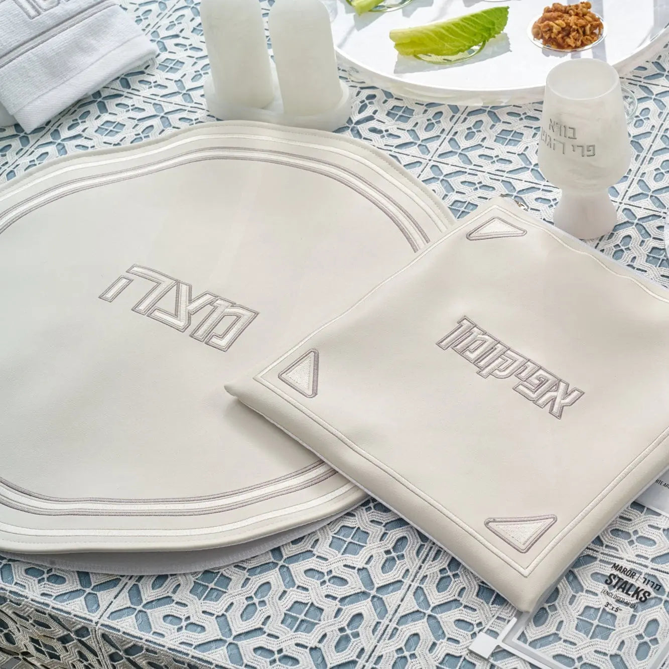 Pearlstone Pesach set featuring white leather plates and matching accessories arranged on blue patterned tablecloth with lettuce and walnuts.