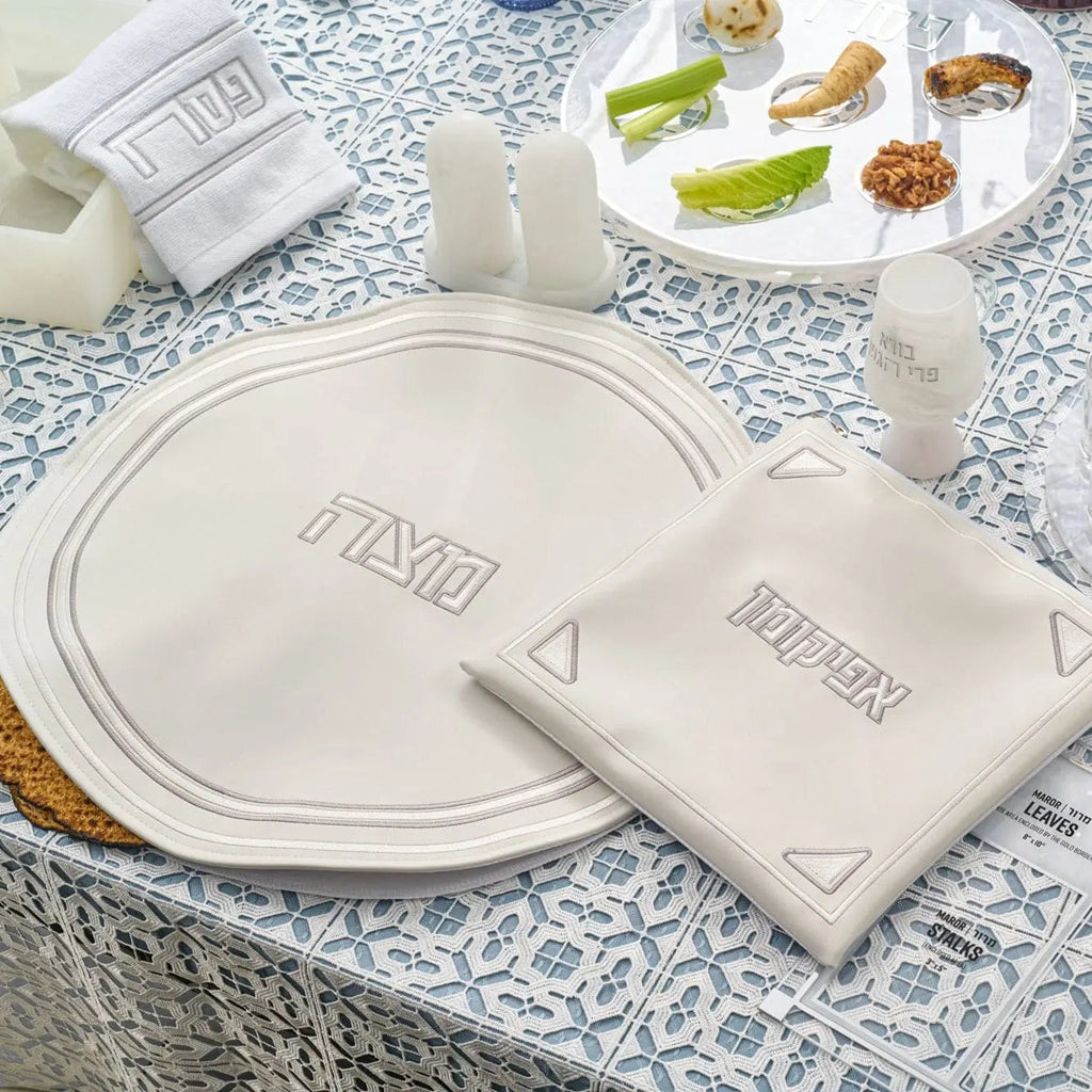 Pearlstone Pesach Set with white pearl marble plates and matching leather napkins arranged on a patterned tablecloth with gold accents.