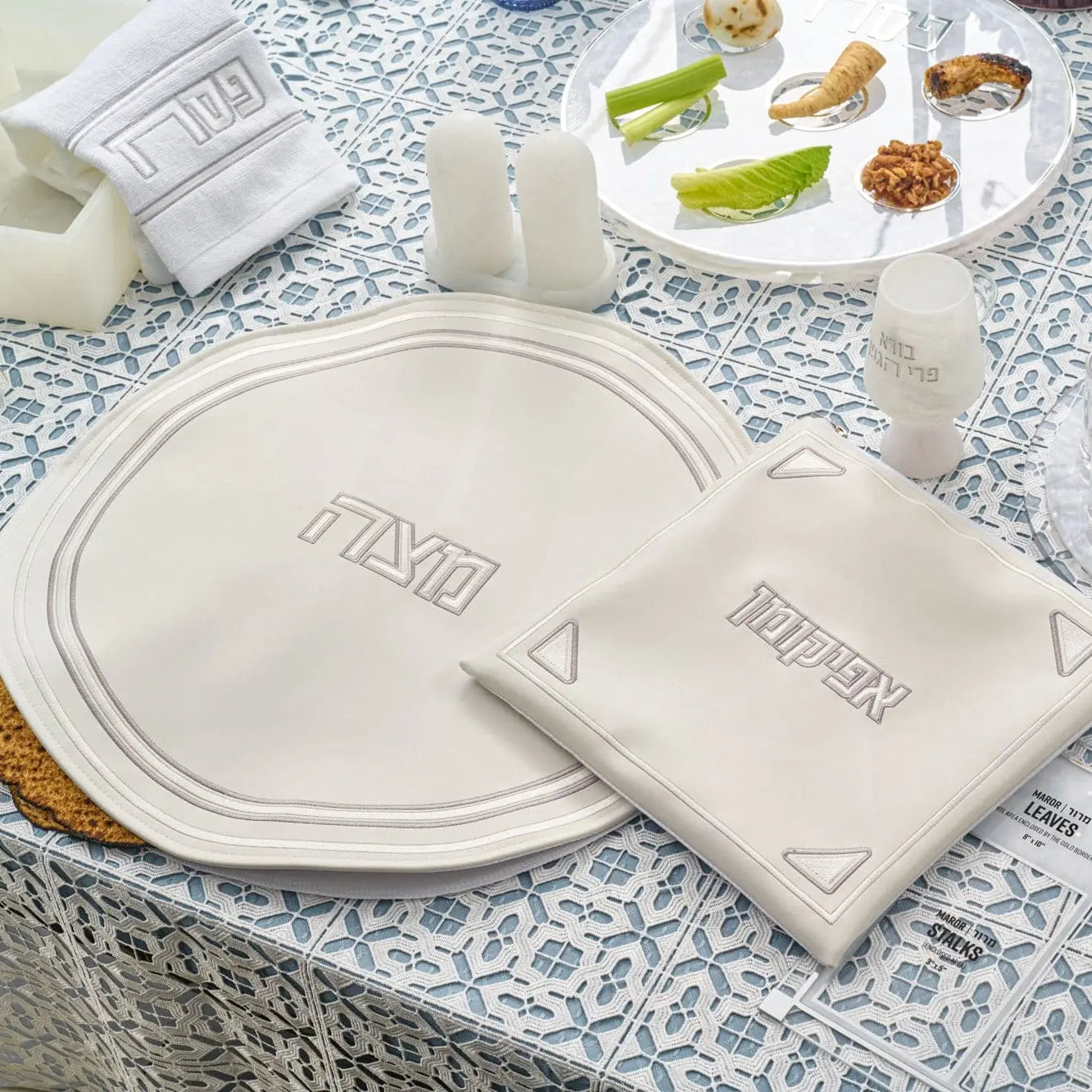 Pearlstone Pesach Set with white pearl marble plates and matching leather napkins arranged on a patterned tablecloth with gold accents.