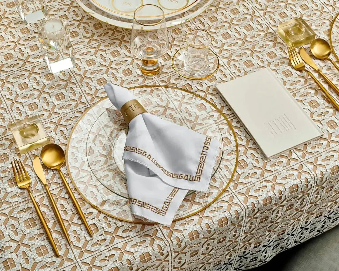 Gold leather Pesach napkin rings arranged on a beige tablecloth with gold flatware and place settings for holiday entertaining.