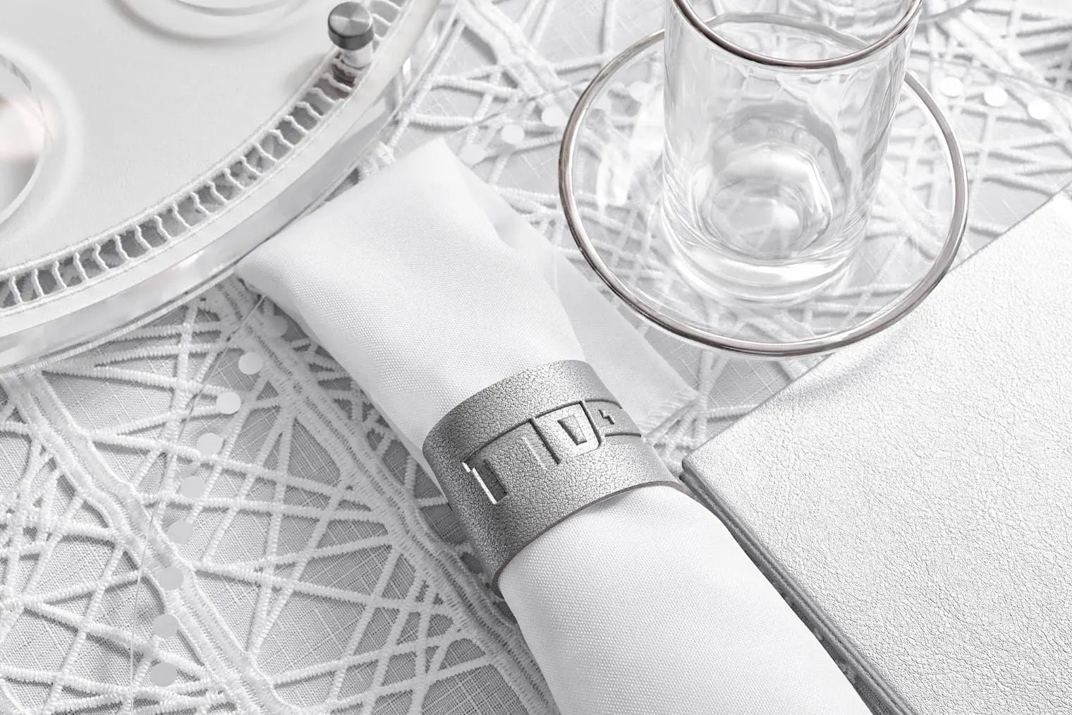 Silver and gold leather Pesach napkin wraps arranged on a white table with decorative napkins and tableware for holiday dining.