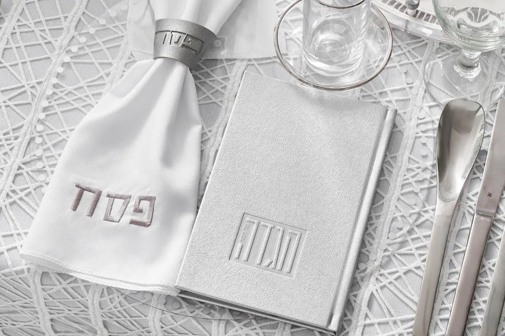 Silver and gold leather Pesach napkin wraps arranged with holiday tableware and place settings on white textured surface