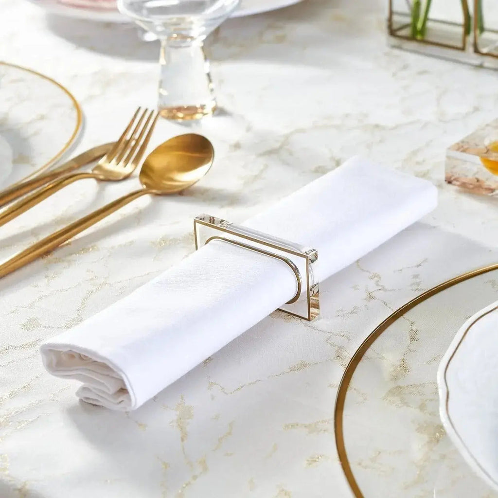 Gold rectangle napkin ring holding a white napkin on a marble table with place setting and gold flatware