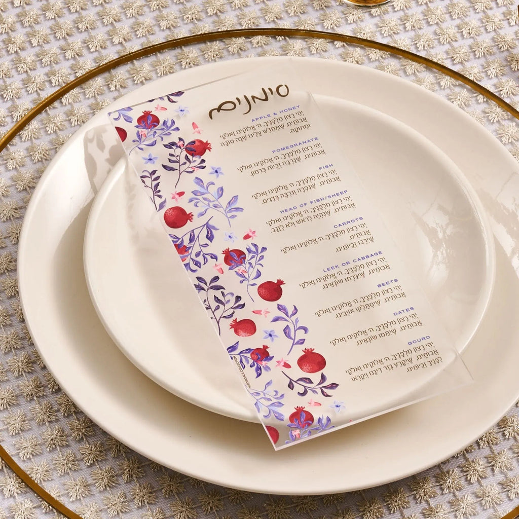 Artistic Simanim Card by Waterdale Collection with floral design printed on clear lucite, displayed on white plates with gold charger for Rosh Hashanah table setting.