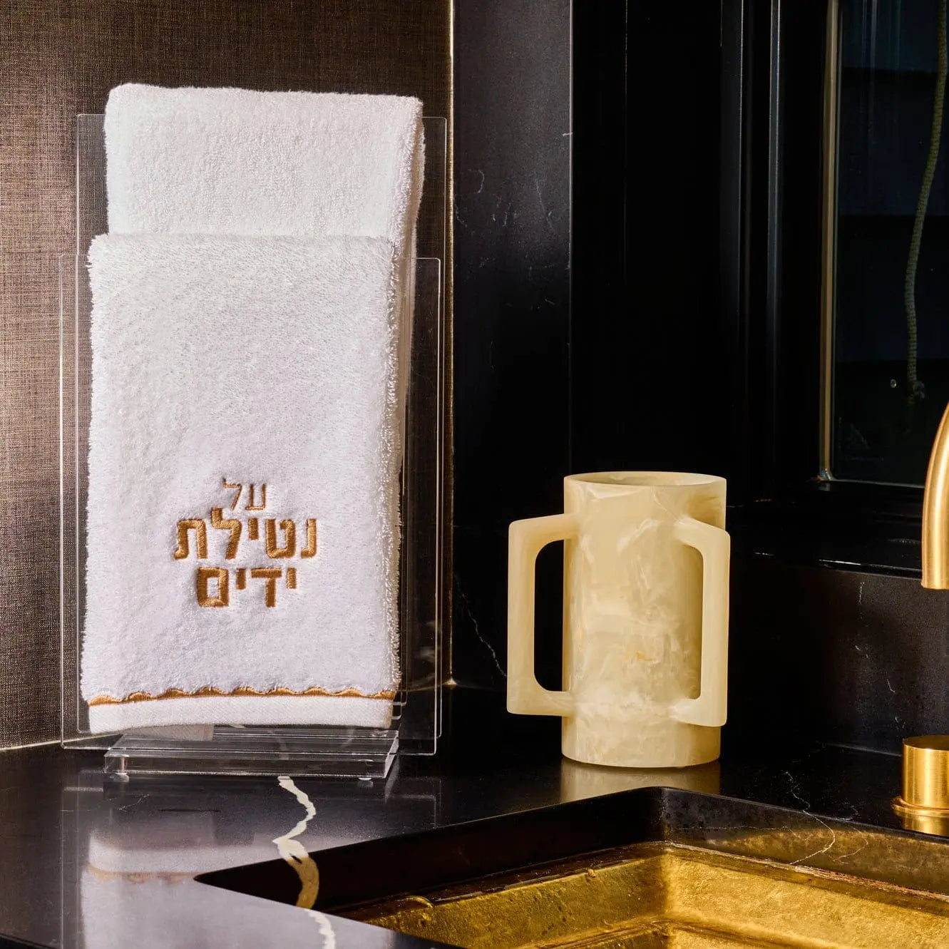 Cream resin washing cup displayed on black surface with gold accents and folded white towel nearby