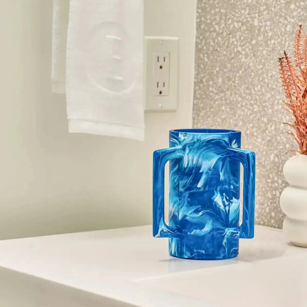Blue marbled resin washing cup displayed on white vanity with decorative coral and white accessories nearby