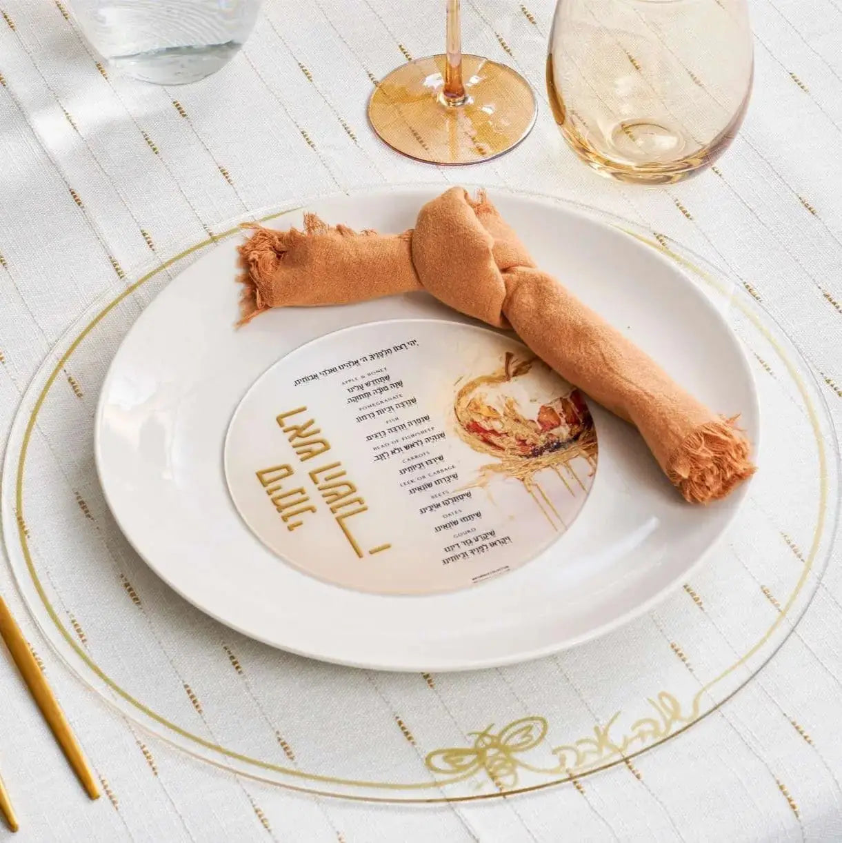 Round Painted Simanim Card by Batya displayed on a white place setting with gold accents, featuring watercolor designs on translucent lucite.