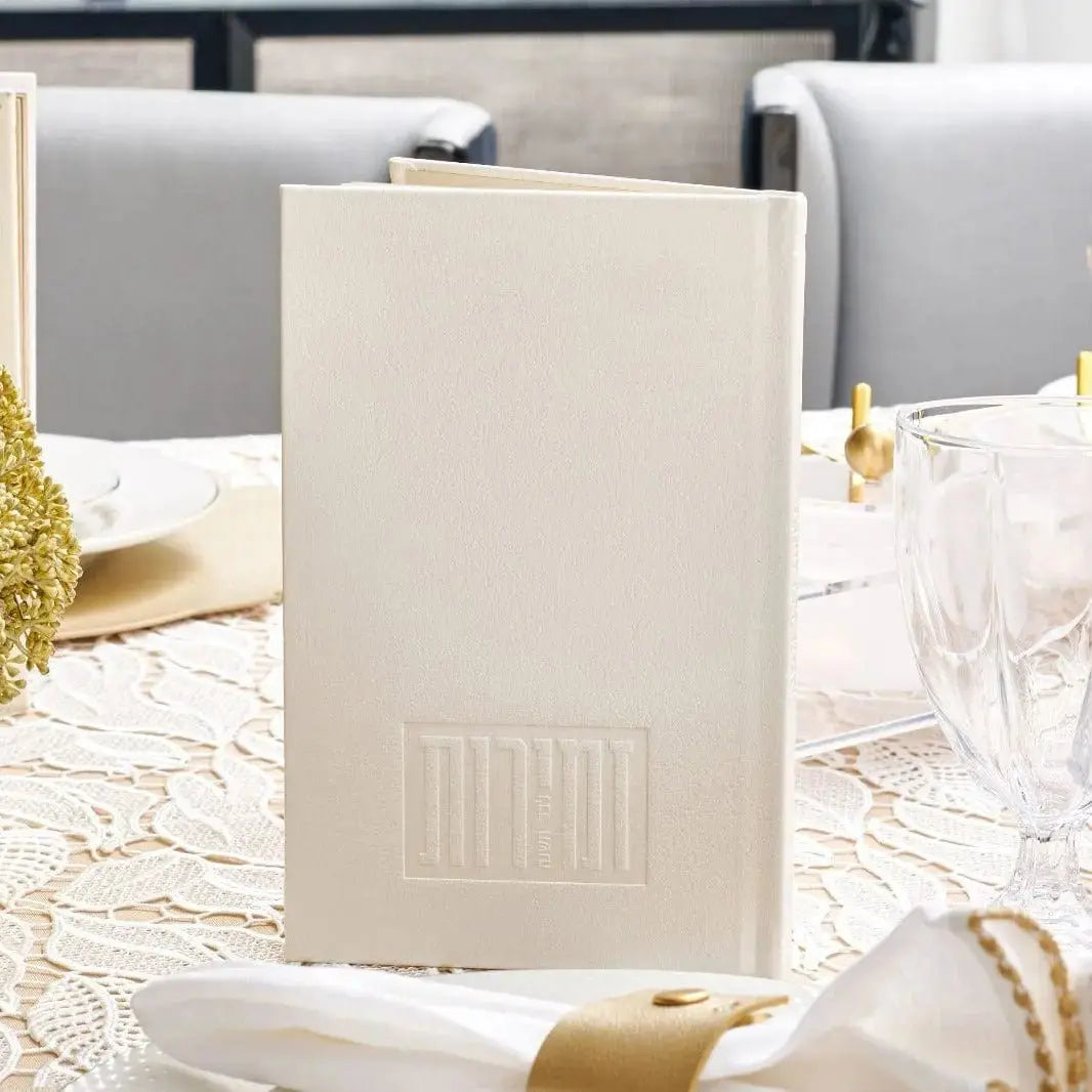Cream-colored Shabbos bencher set of six prayer books displayed on a white table with gold decorative accents and greenery.