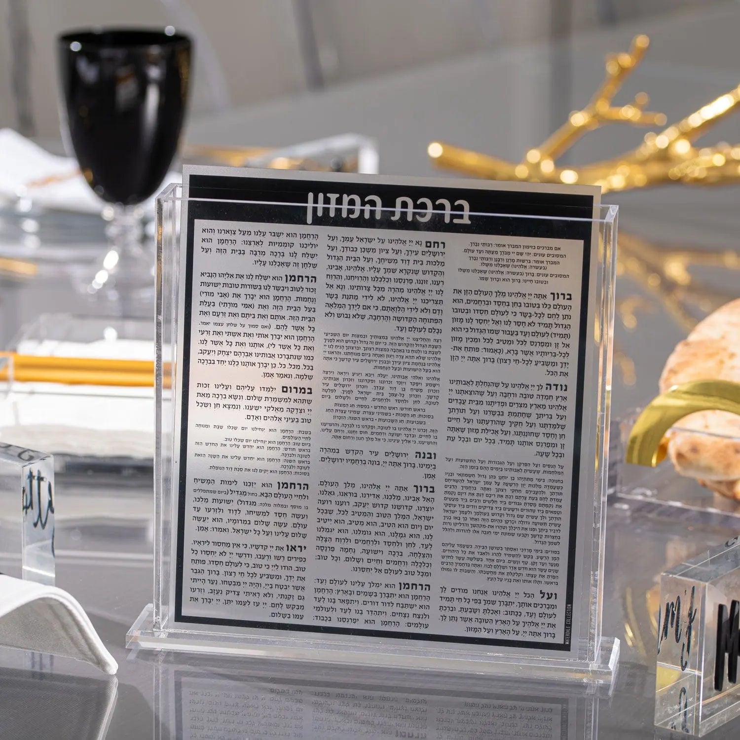 Black and silver Square Bencher Set on display table with wine glass and holiday decorations, Waterdale Collection Shabbat bencher.