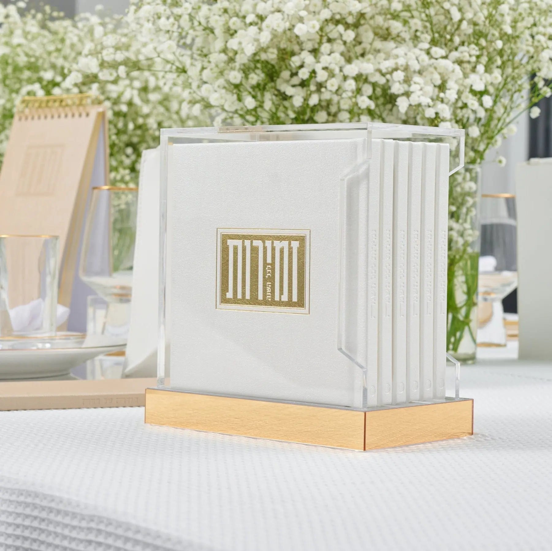 White and gold Square Shabbos Zemiros Bencher Set displayed on wooden base with greenery backdrop, ideal for Shabbat table settings