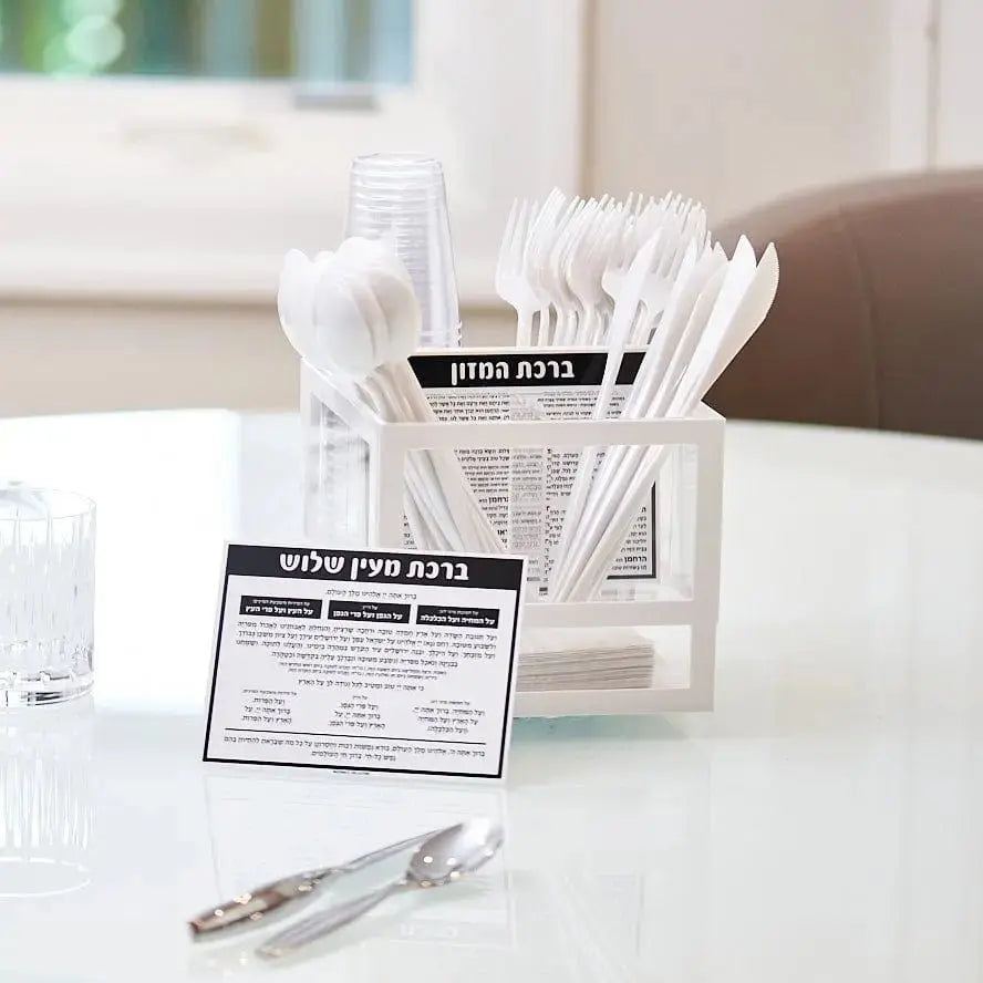 Waterdale Collection Sukkos card displayed in clear plastic silverware caddy with white plastic utensils on white table.