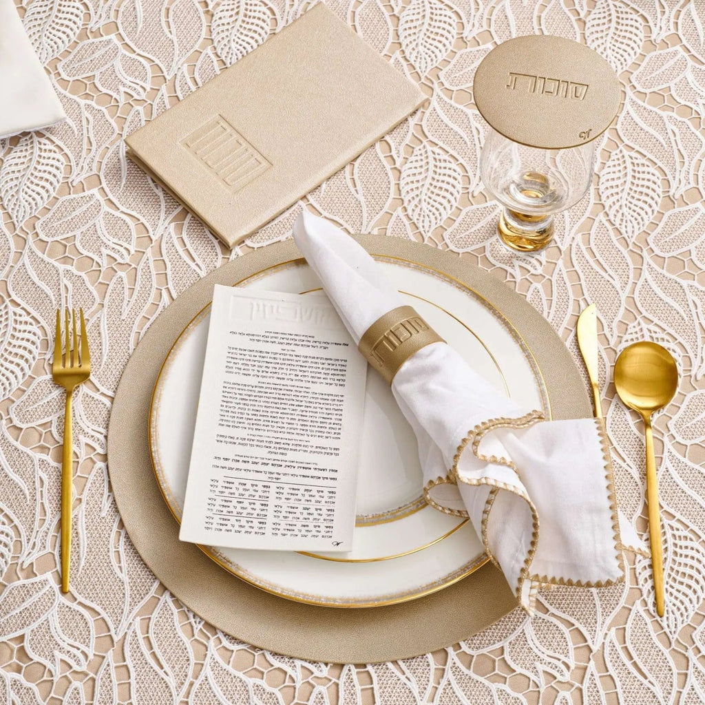 Gold leather napkin wraps from Waterdale Collection arranged on place setting with white linens and gold flatware for elegant Sukkot table décor.