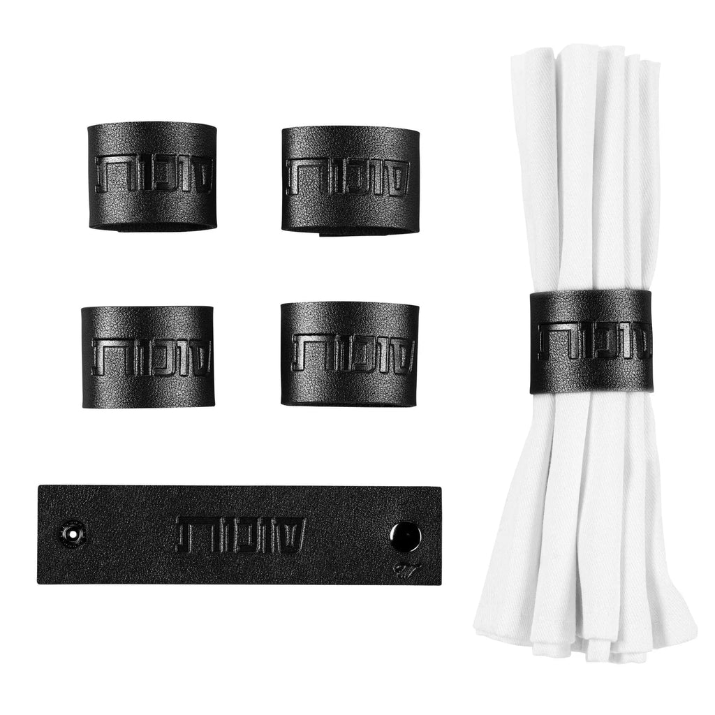 Sukkos Leather Napkin Wraps in black leatherette with silver and gold metal rings, displayed with white napkins and packaging.