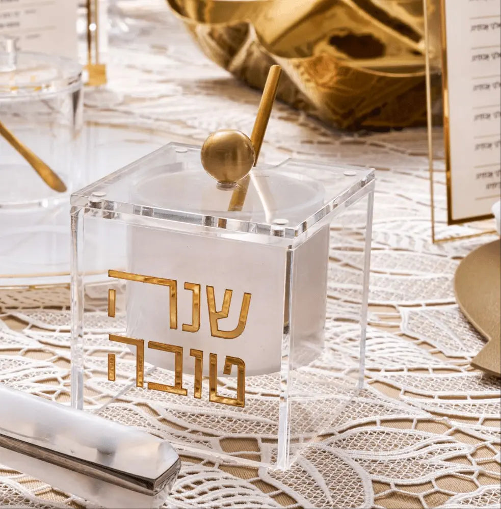 Suspended honey dish in gold-toned metal with geometric cutout design, displayed on white marble surface with holiday decor.