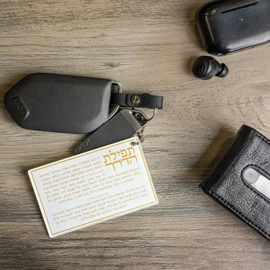 Black Tefillas Haderech keychain with pocket-sized prayer card displayed on wooden surface alongside other items