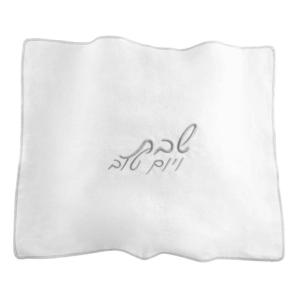 White linen challah cover with embroidered Hebrew text, traditional Shabbat table setting accessory from Waterdale Collection.