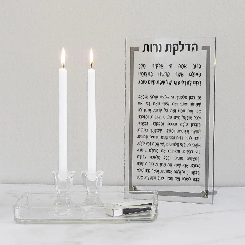 Glass tabletop Hadlokas Neiros plaque with Hebrew text, paired with crystal candlestick holders and two lit white candles for Shabbat.