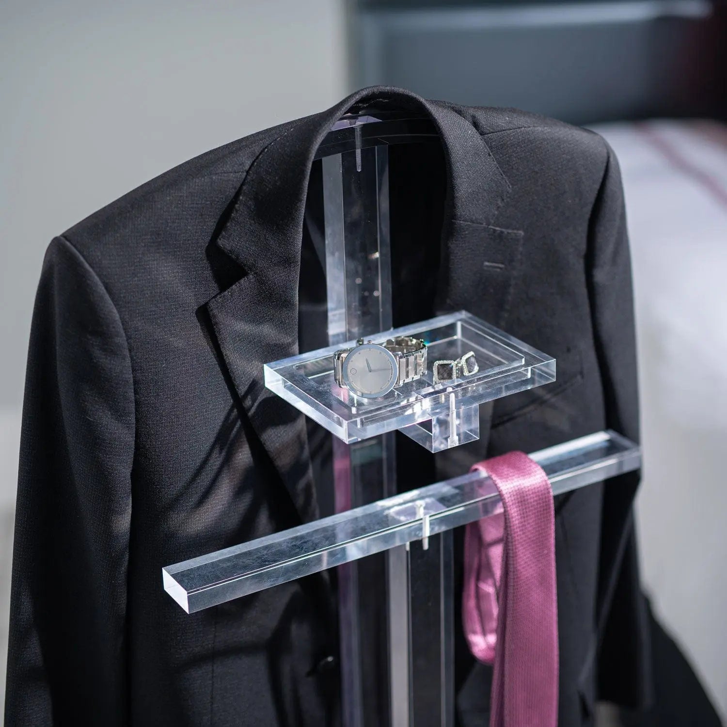 Black valet stand with hanging bar displaying formal jacket, tie, and accessories for organized men's clothing storage