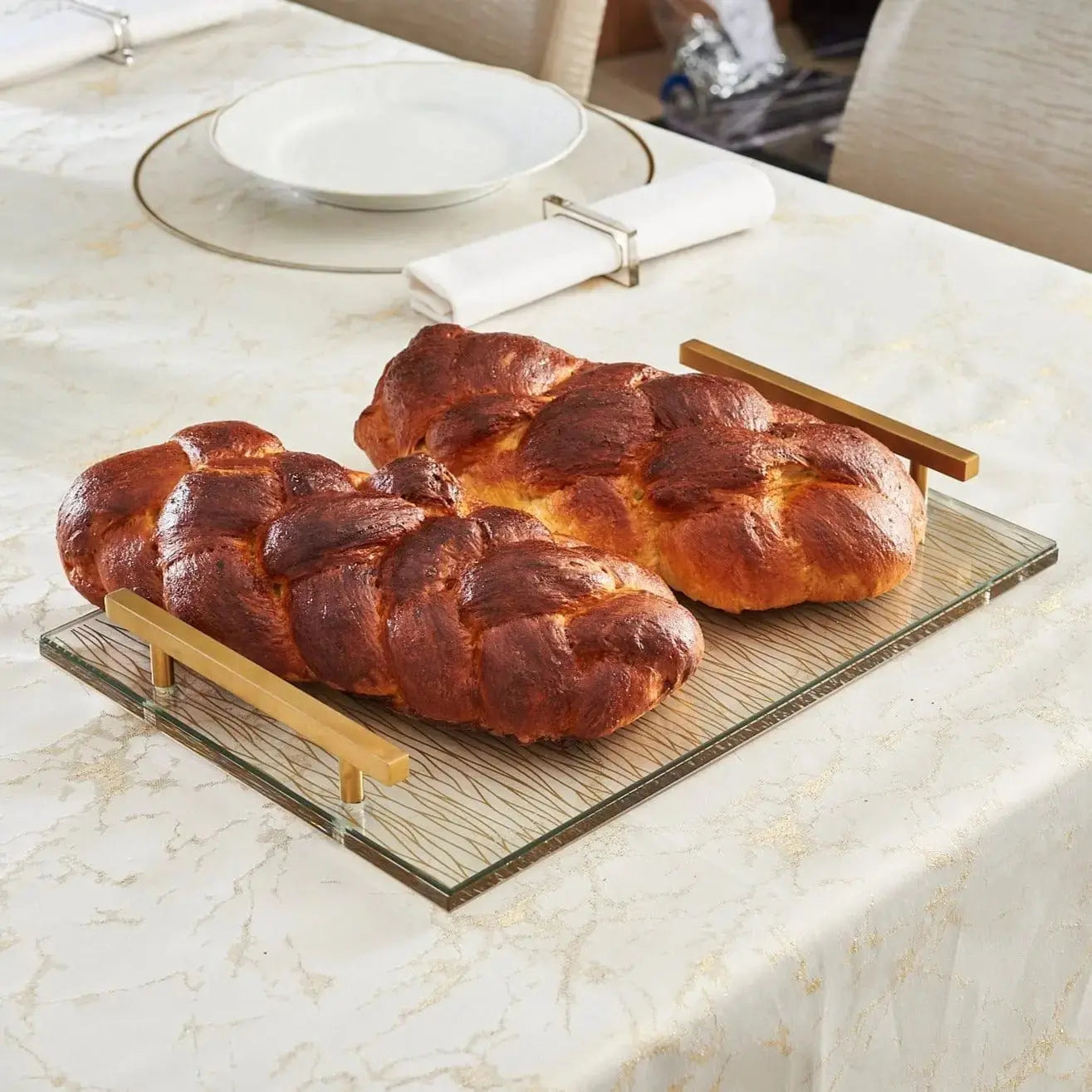 Wave Challah Board by Waterdale Collection in silver, displayed with braided challah bread on a marble table setting for Shabbat.